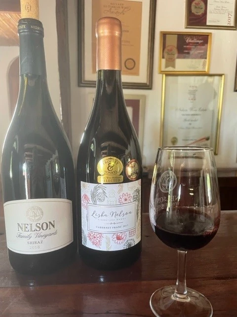 Two red wine bottles and a filled wine glass on table