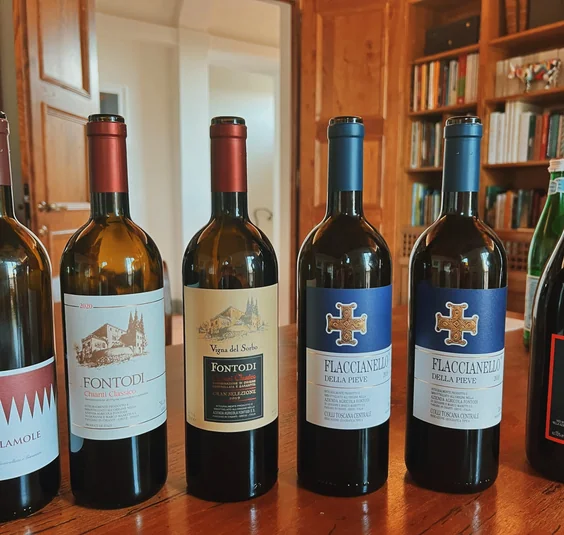 Six bottles of Italian wine, including Fontodi Chianti Classico and Flaccianello della Pieve, on a wooden table
