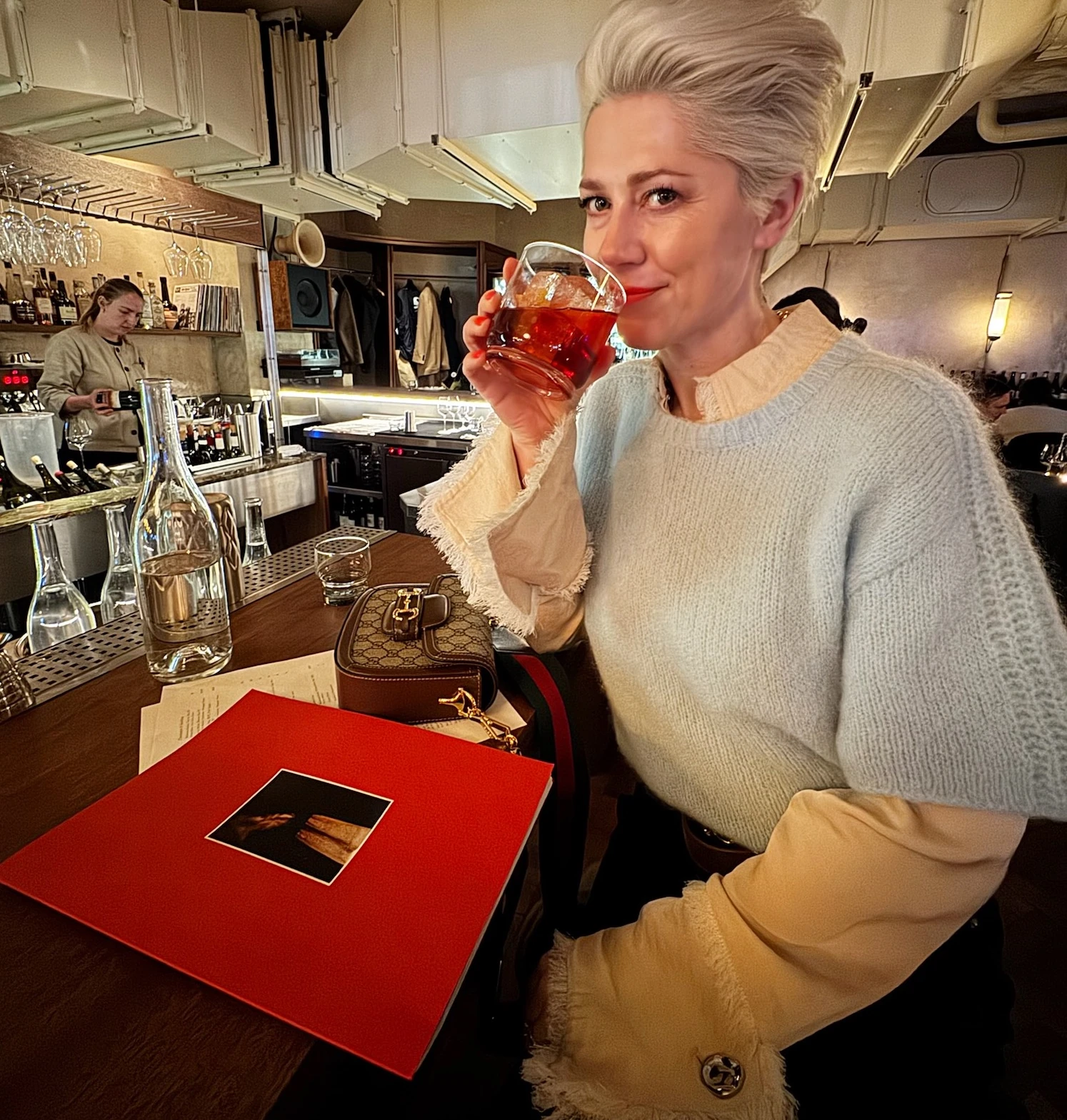 Guest sipping a red drink at a stylish bar with wine glasses and bottles