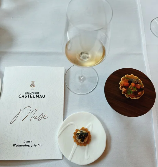 Champagne Castelnau menu, wine glass and canapés on a white table