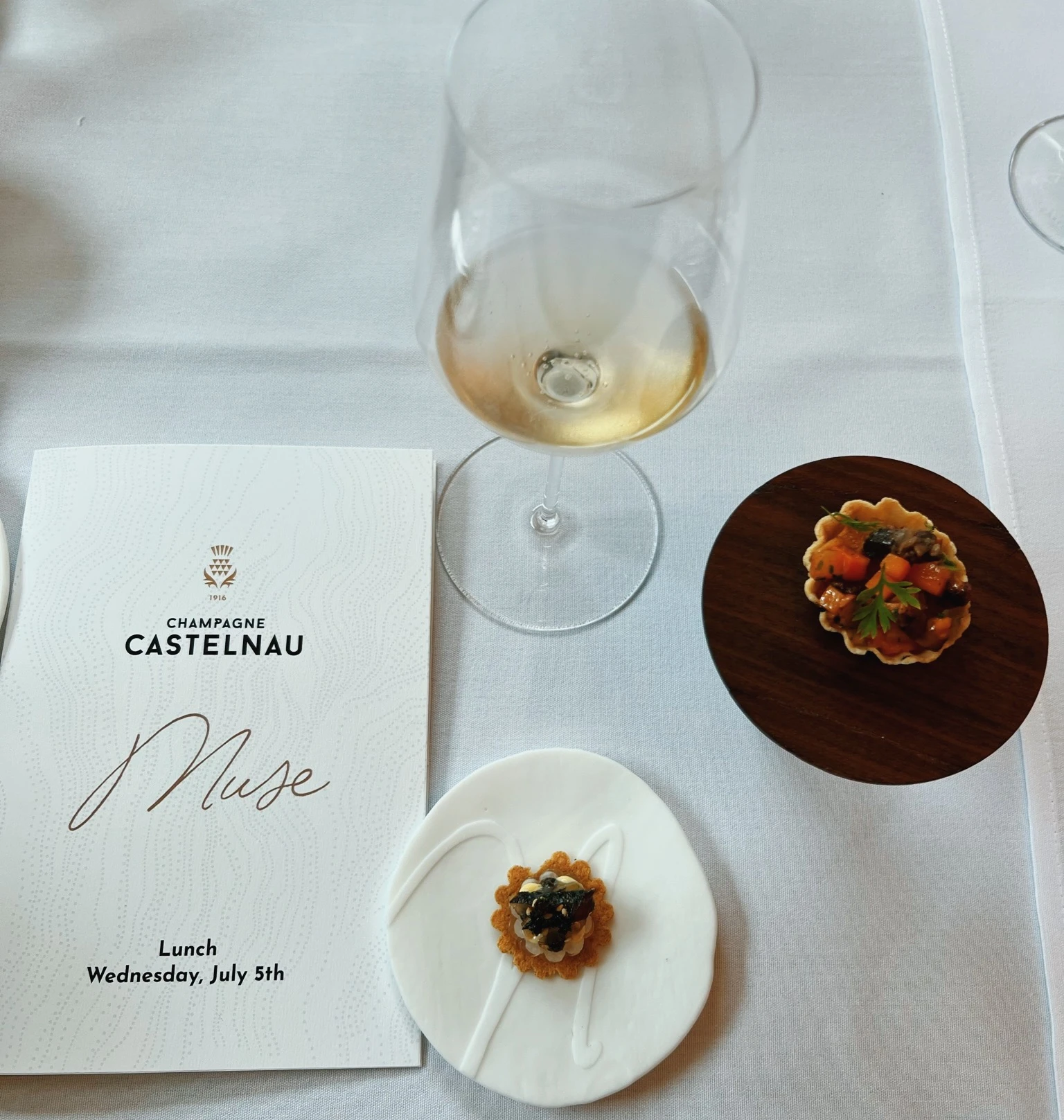 Champagne Castelnau menu, wine glass and canapés on a white table
