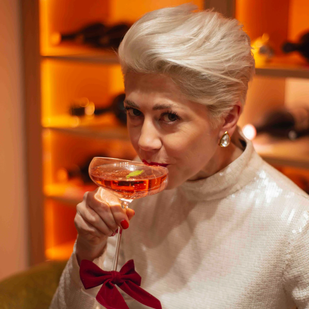 Woman with short blonde hair sipping a cocktail in a coupe glass
