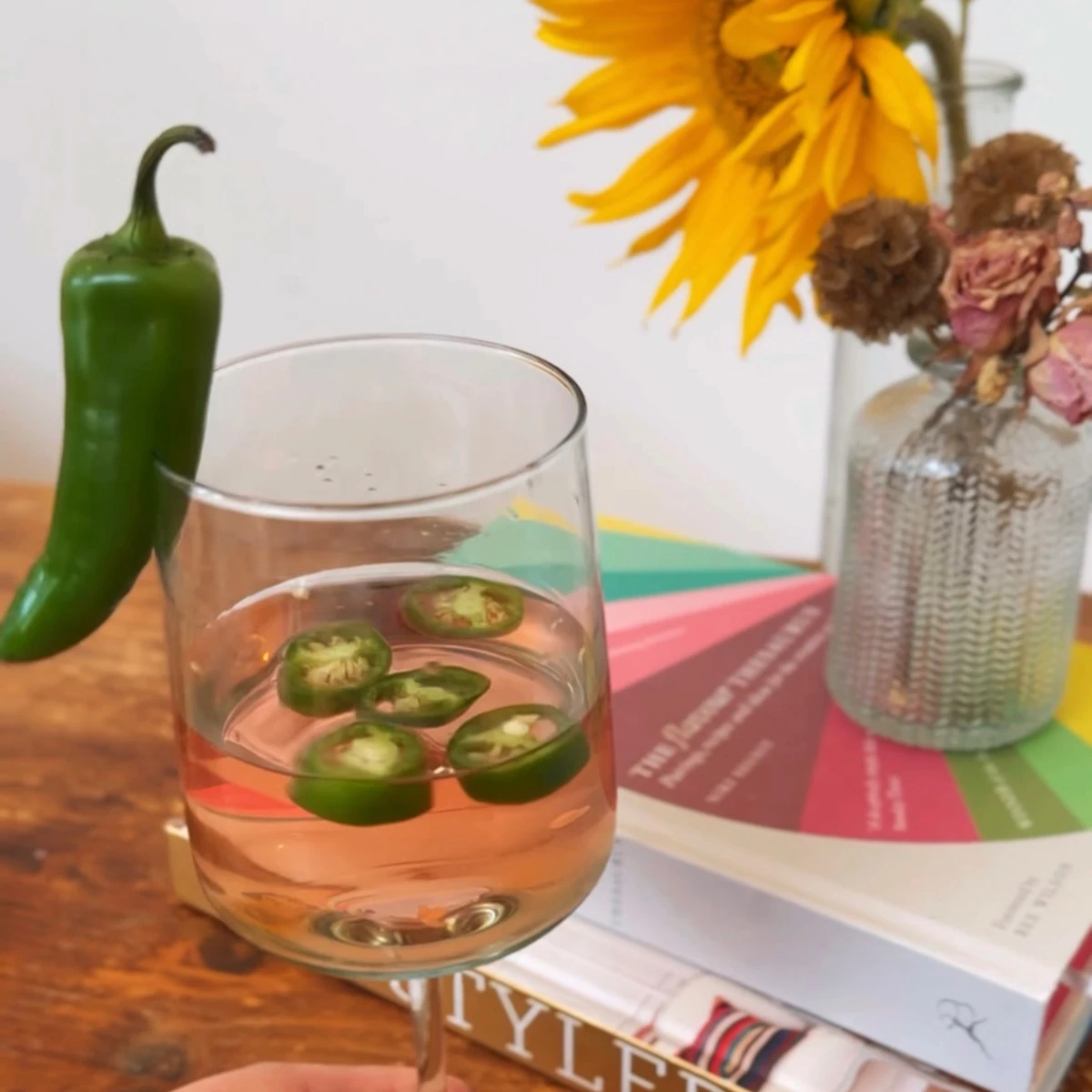 Rosé wine with sliced chillies beside a whole chilli, flowers and colourful books