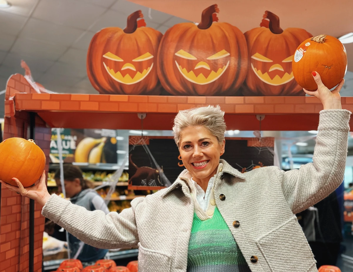 Woman holding two pumpkins beneath three jack-o'-lantern decorations