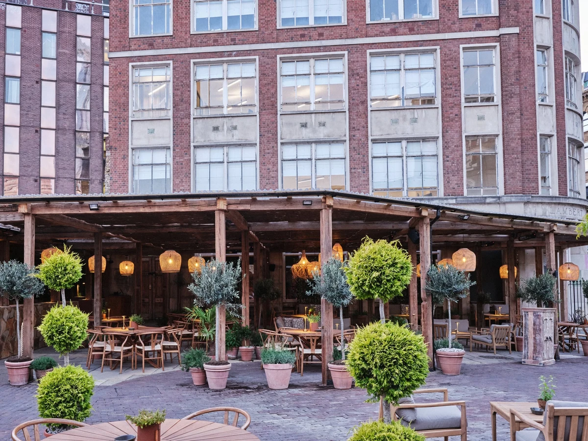 Outdoor restaurant terrace with potted topiary trees beneath a brick building