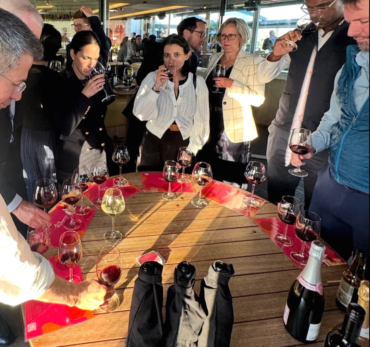 People tasting wine around a table with glasses and covered bottles