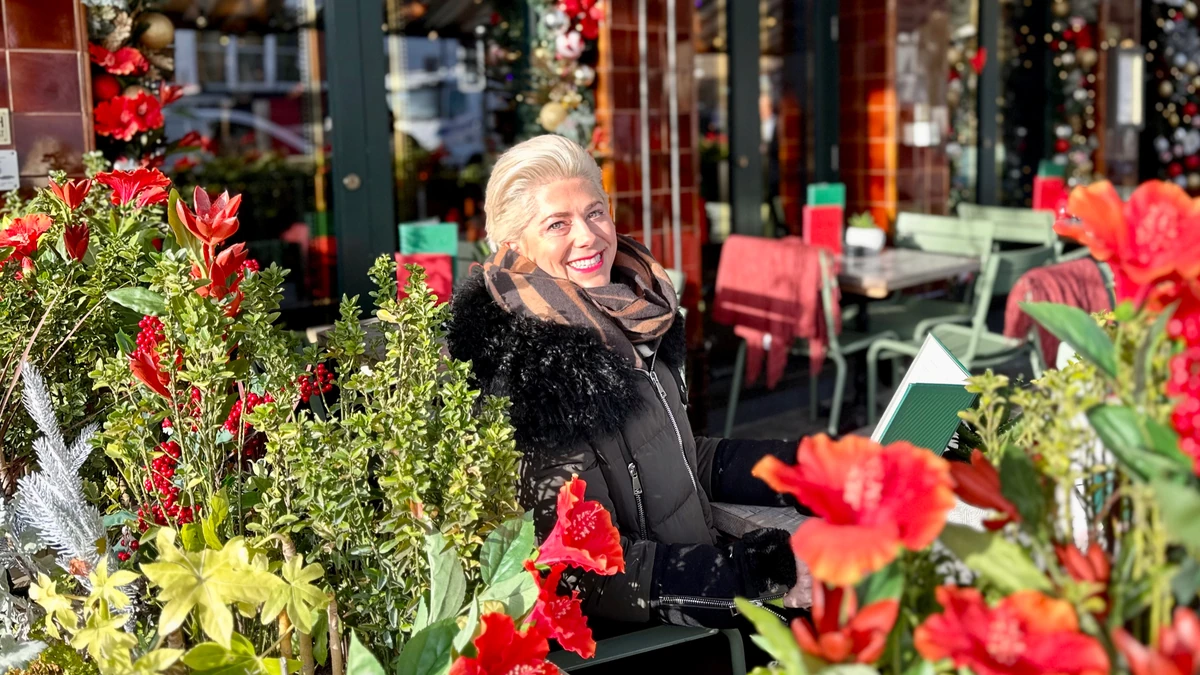 Smiling woman seated outside a café, surrounded by vibrant red flowers and festive decorations
