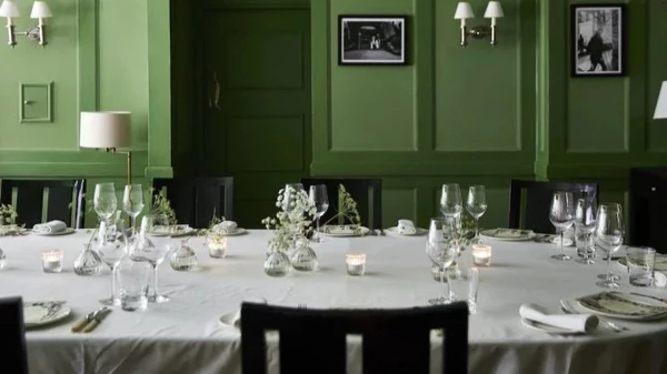 Elegant dining table set with wine glasses, floral centrepieces and candles in green room