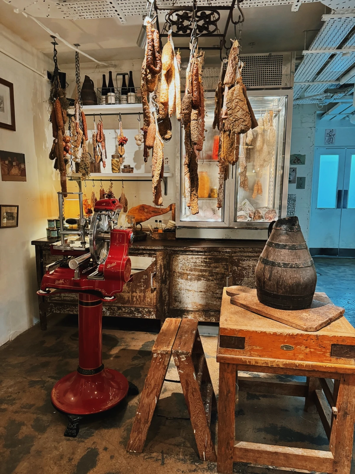 Hanging cured meats, red slicer and wooden barrel in a rustic food shop