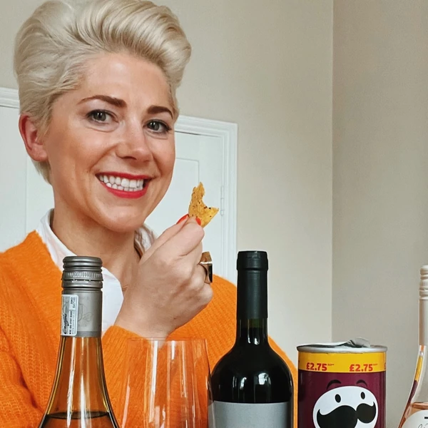 Smiling woman holding a crisp beside wine bottles and glasses