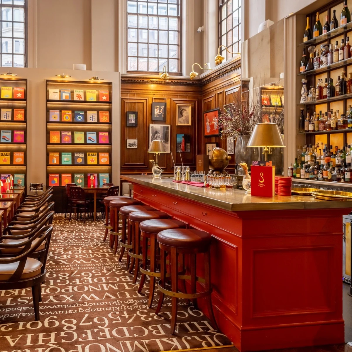 Elegant bar with red counter, stools, drinks shelves, framed art and patterned carpet