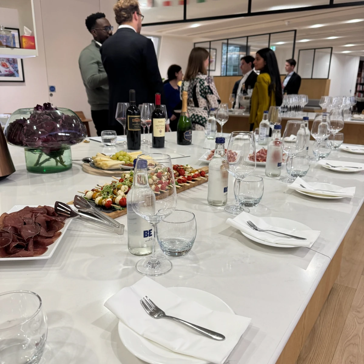 Wine tasting event with guests, wine bottles, glasses, water and food arranged on tables