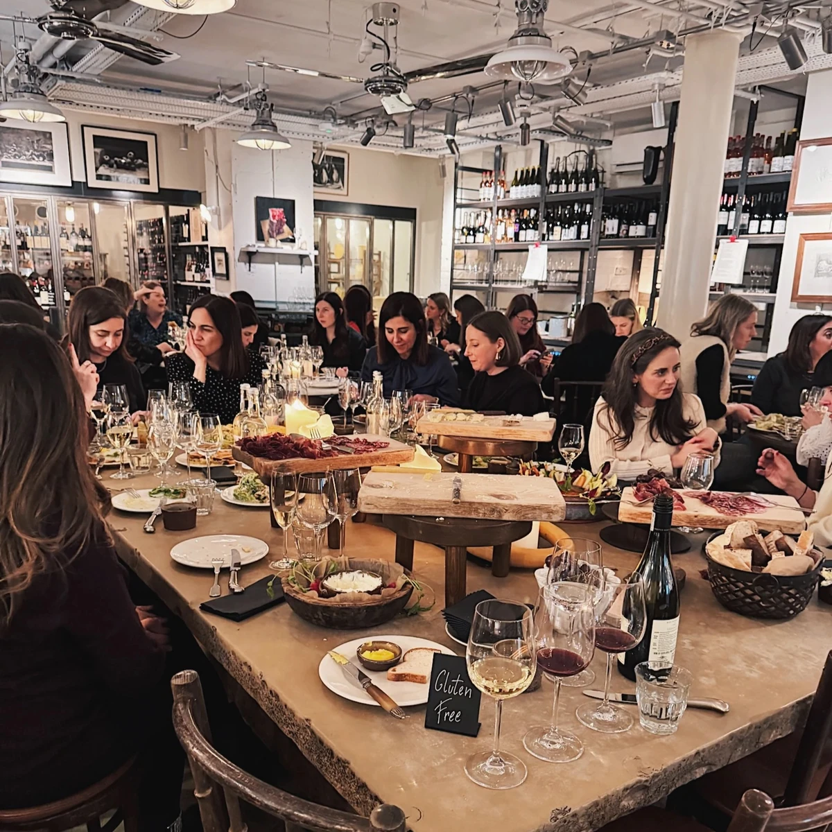 Diners sharing wine and food at a busy restaurant table with a Gluten Free sign