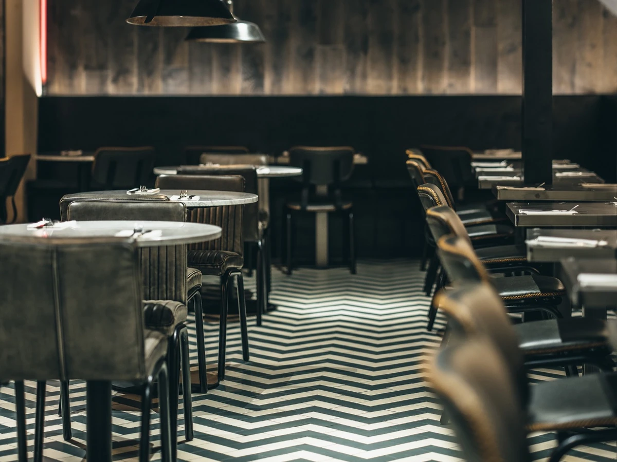 Empty restaurant dining room with set tables, pendant lights and black-and-white chevron flooring