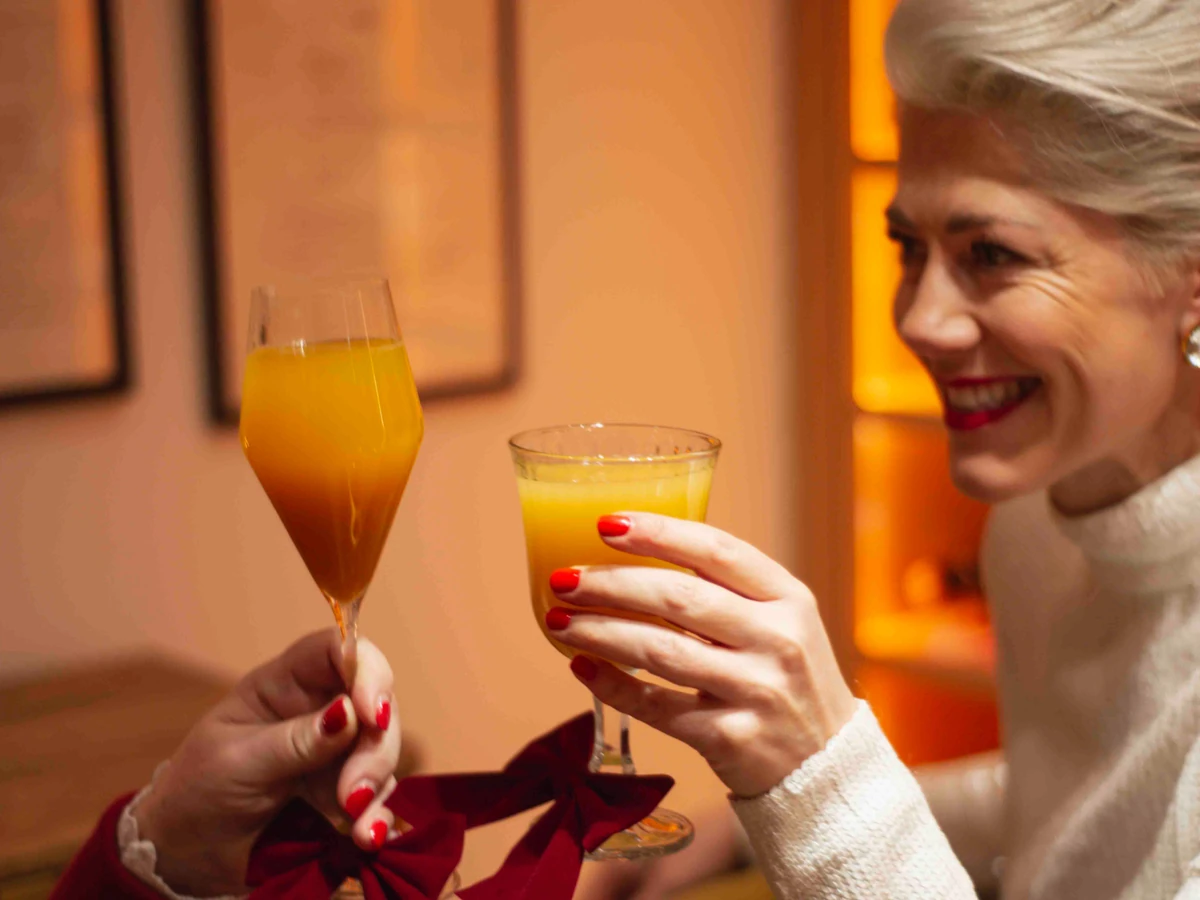 Smiling woman holding a glass of orange drink beside another raised glass