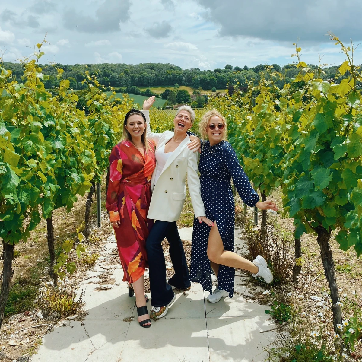 Three women smiling and posing among vineyard vines with rolling countryside behind them