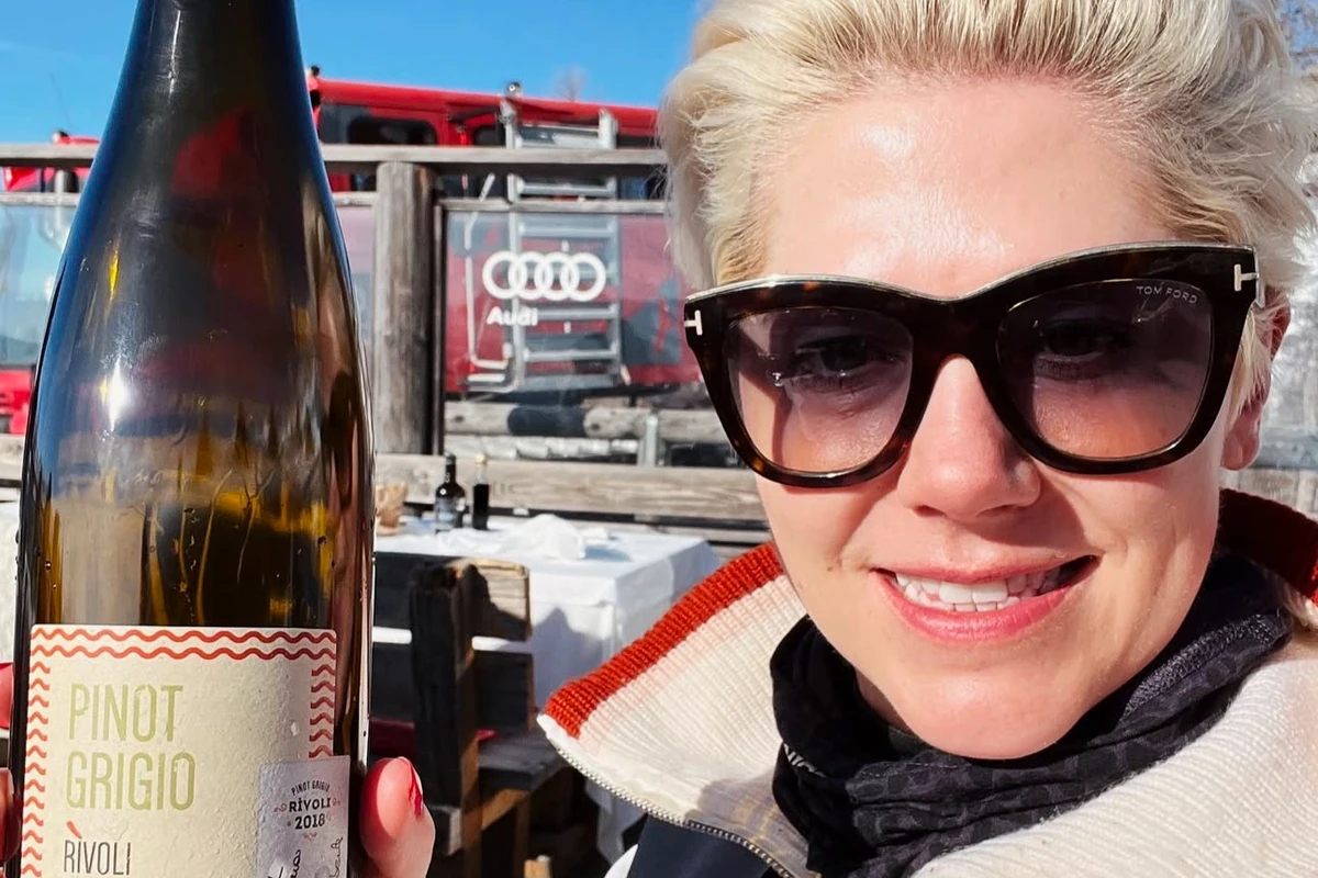 Woman holding a Pinot Grigio wine bottle outdoors wearing sunglasses