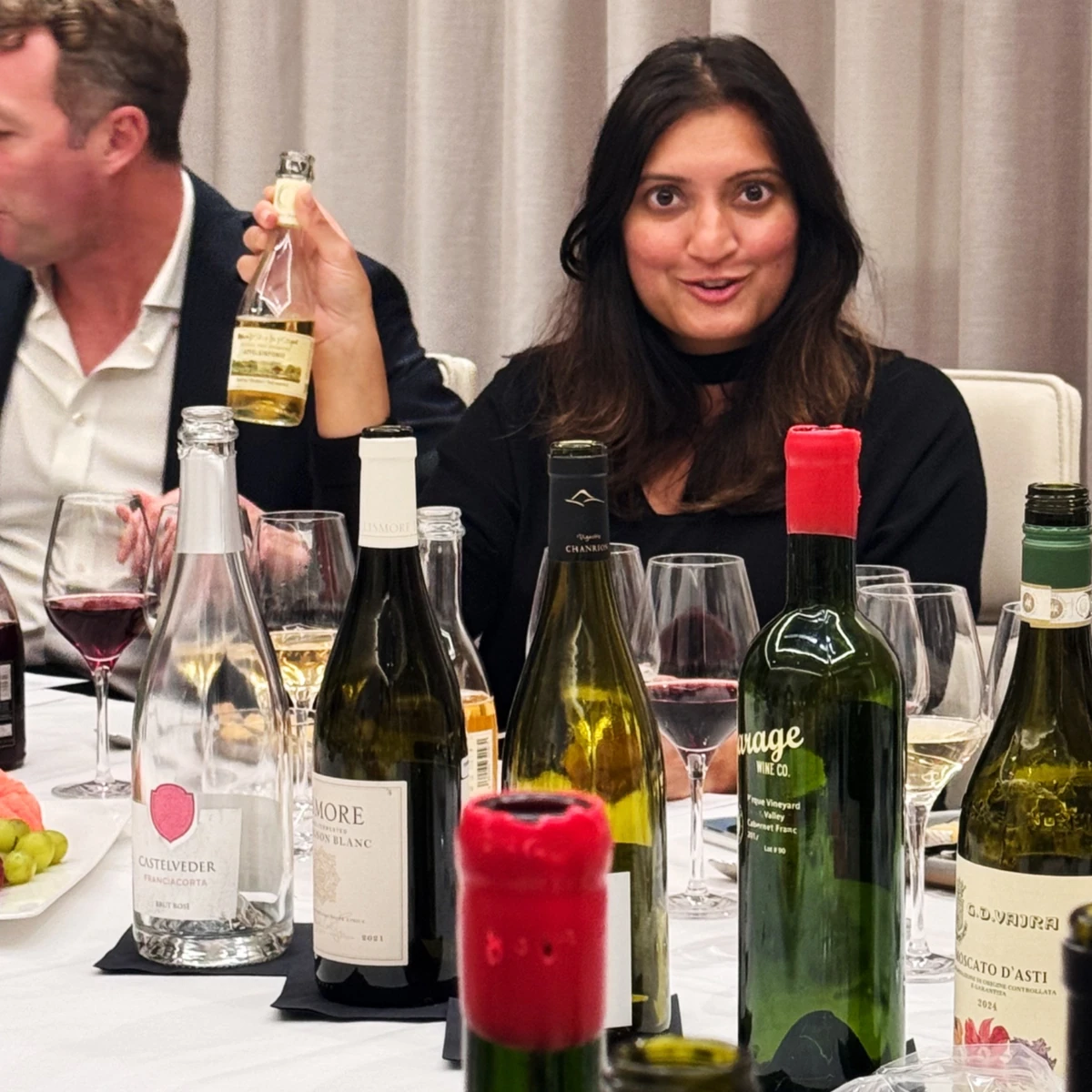 Woman holding a wine bottle at a tasting table with bottles and glasses