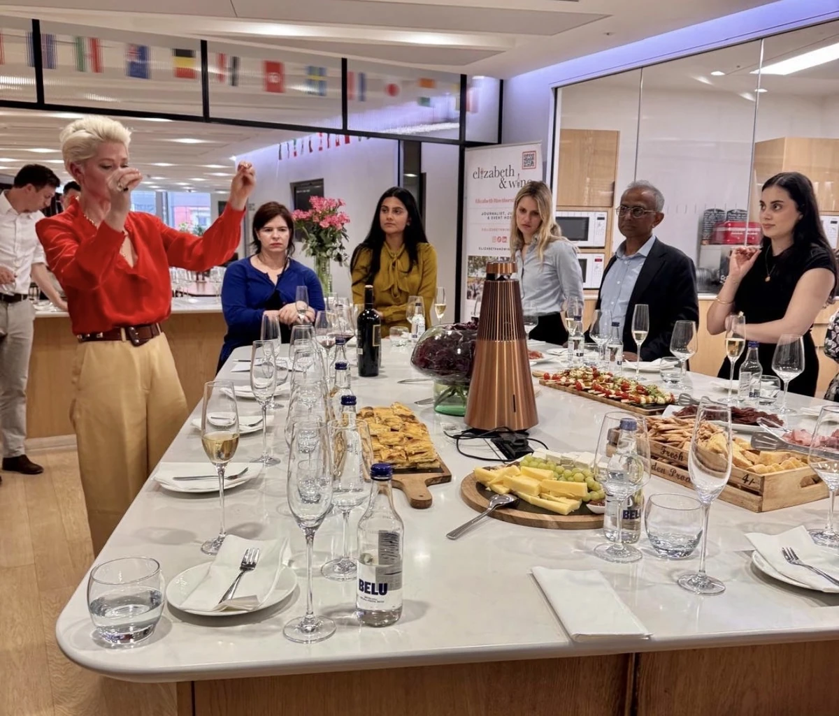 People gathered around a table with wine glasses, food and a presenter