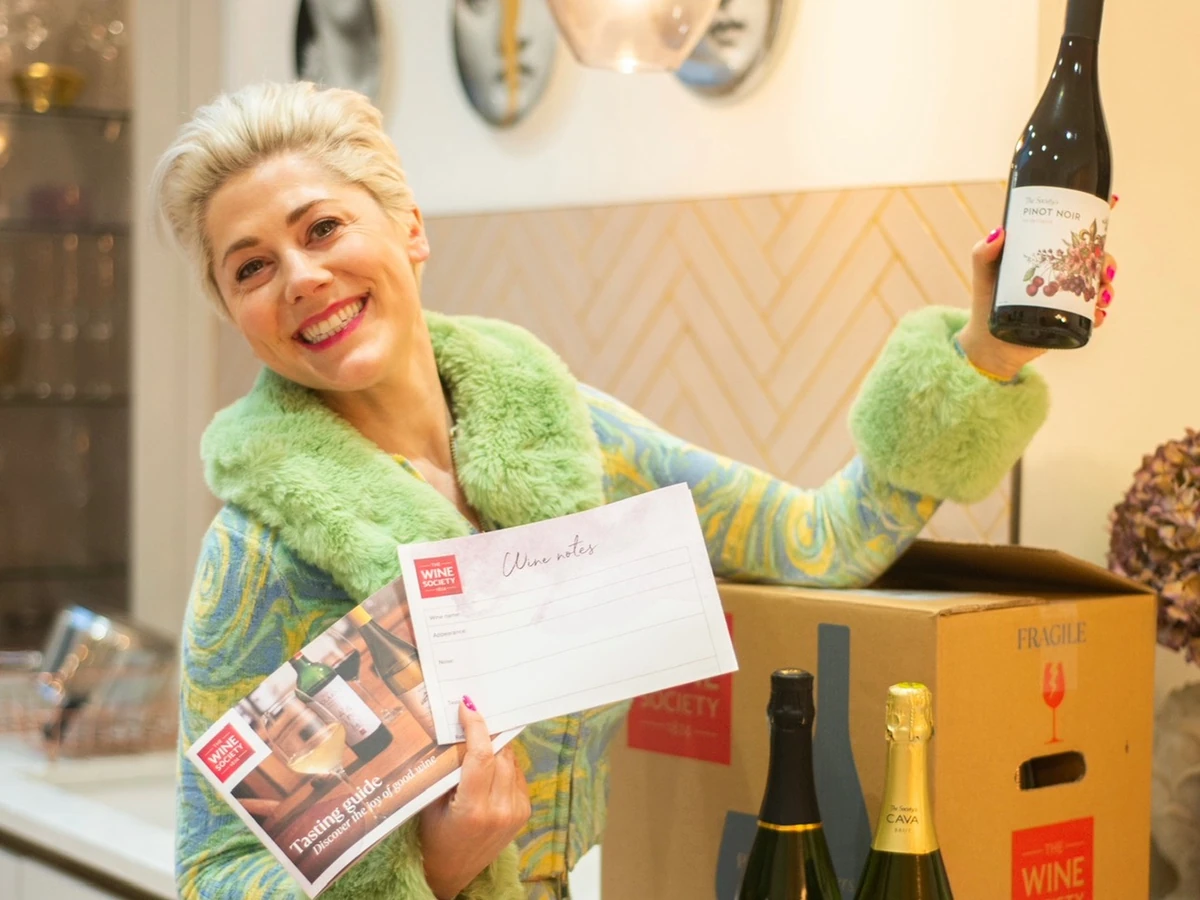 Smiling woman holding a Pinot Noir bottle, wine brochures and boxes