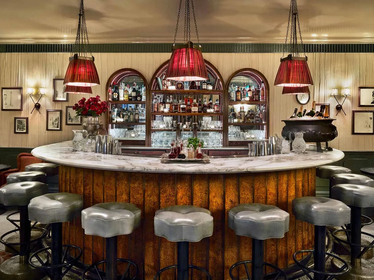 Elegant cocktail bar with red pendant lights, marble counter, bottles and grey stools