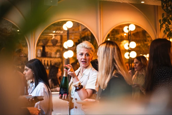 Woman holding a wine bottle among guests at an indoor event