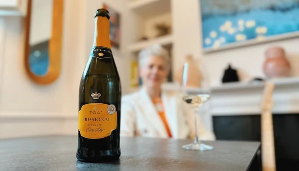 Bottle of Prosecco on a table with a blurred person and wine glass behind