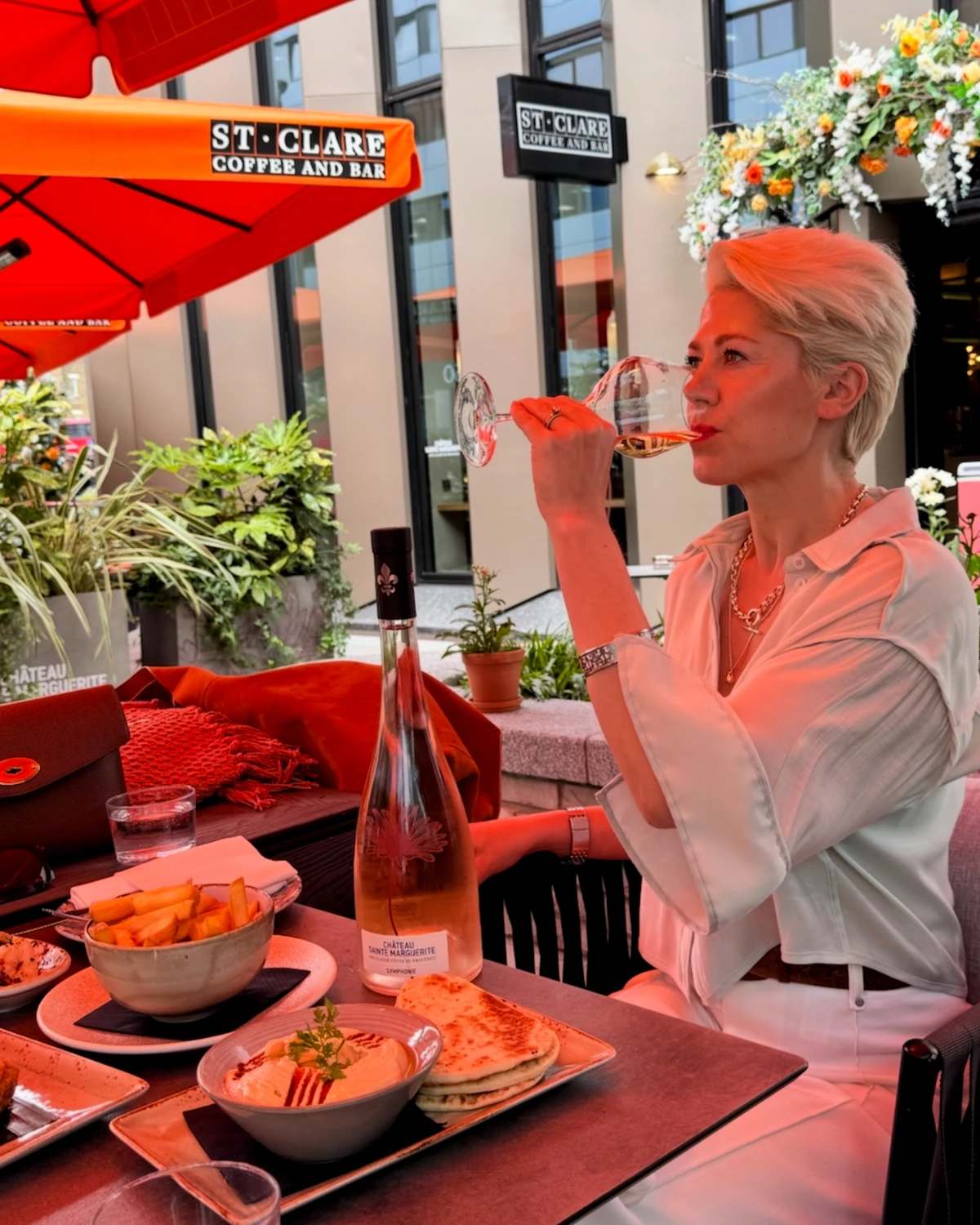 Woman sipping wine at an outdoor cafe table with food