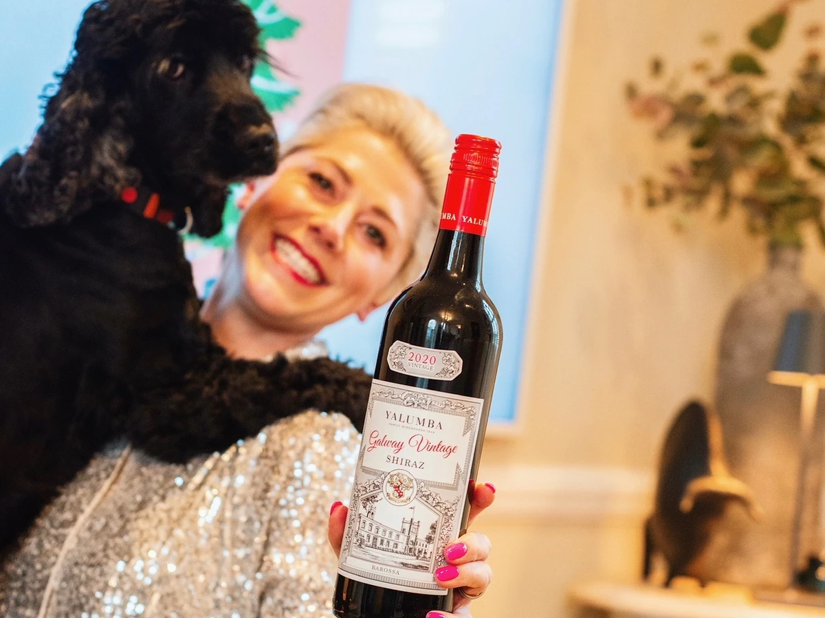 Woman holding Yalumba Galway Vintage Shiraz wine bottle beside black dog