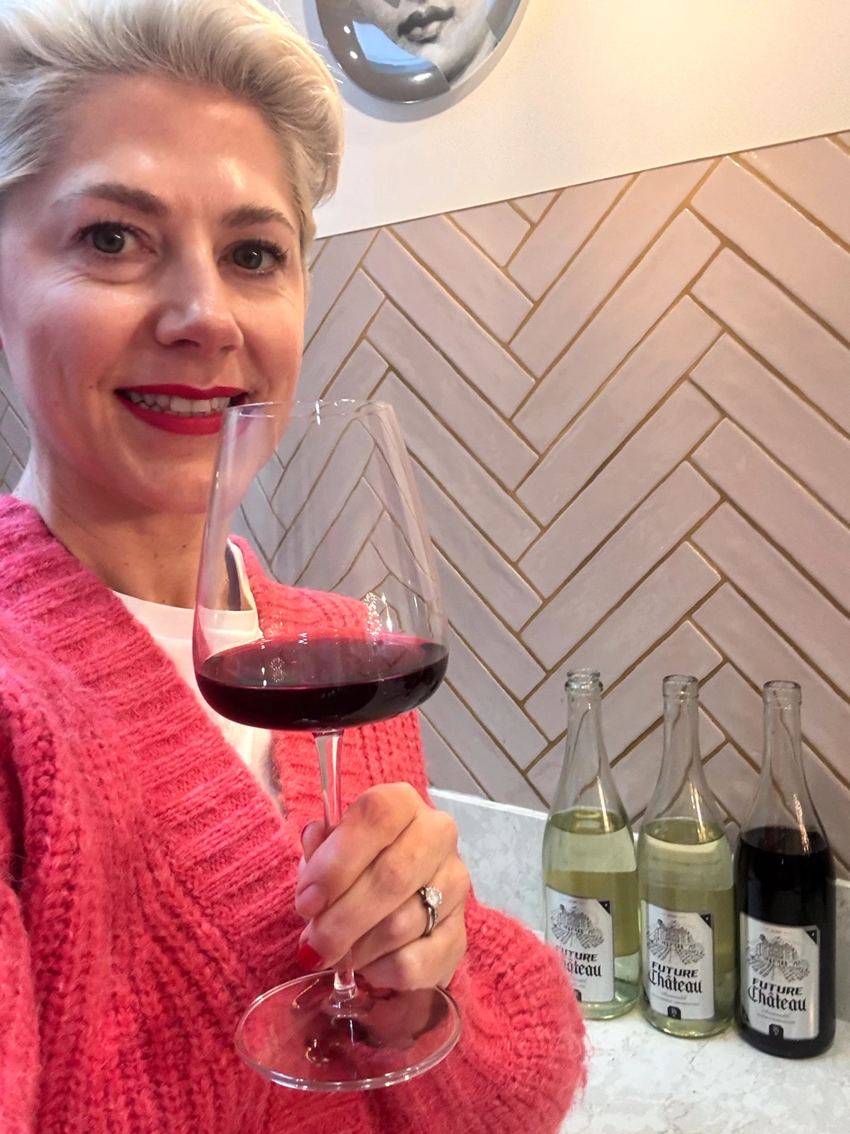 Woman in pink jumper holding red wine glass beside Future Château wine bottles