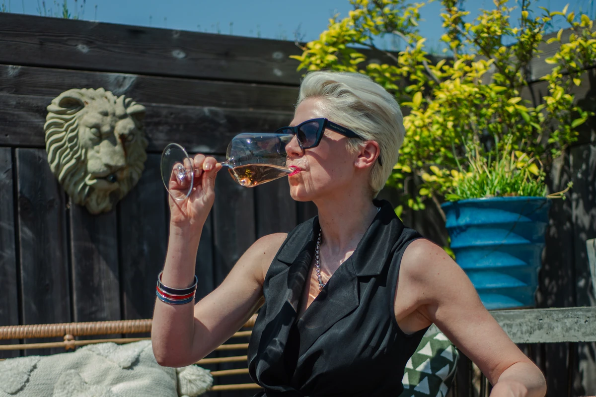 Woman wearing sunglasses drinking wine outdoors beside a lion wall ornament