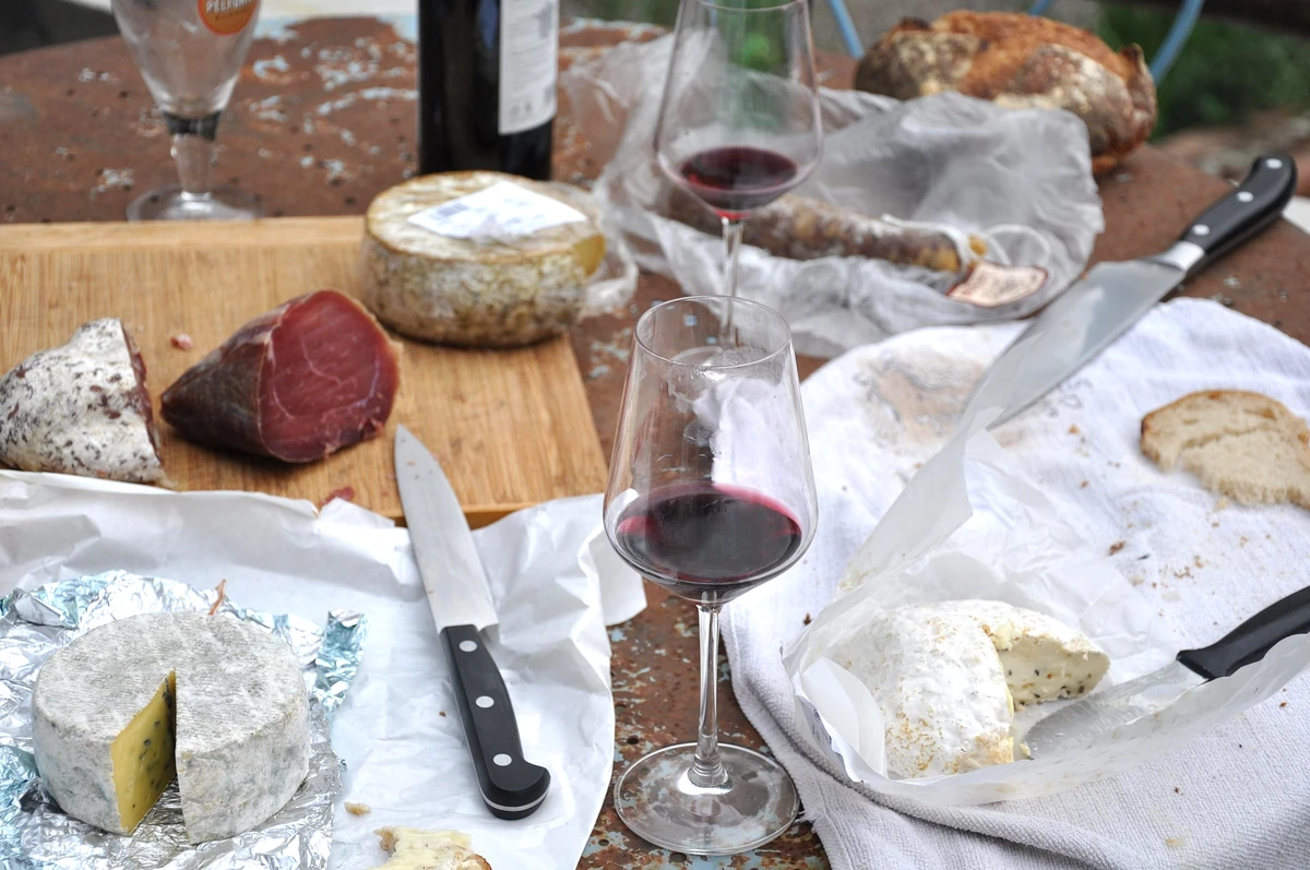 Red wine, cheeses, cured meats, bread and knives arranged on a table