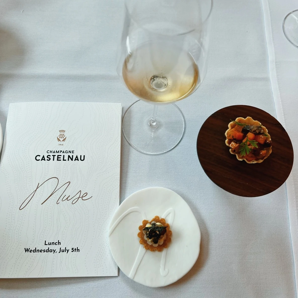 Wine glass, plated appetisers and Champagne Castelnau Muse lunch menu reading Wednesday, July 5th