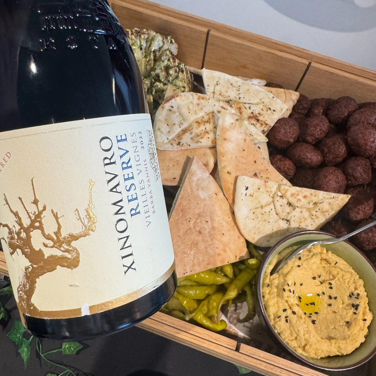 Wine bottle beside flatbreads, meatballs, hummus and green peppers in a wooden serving tray