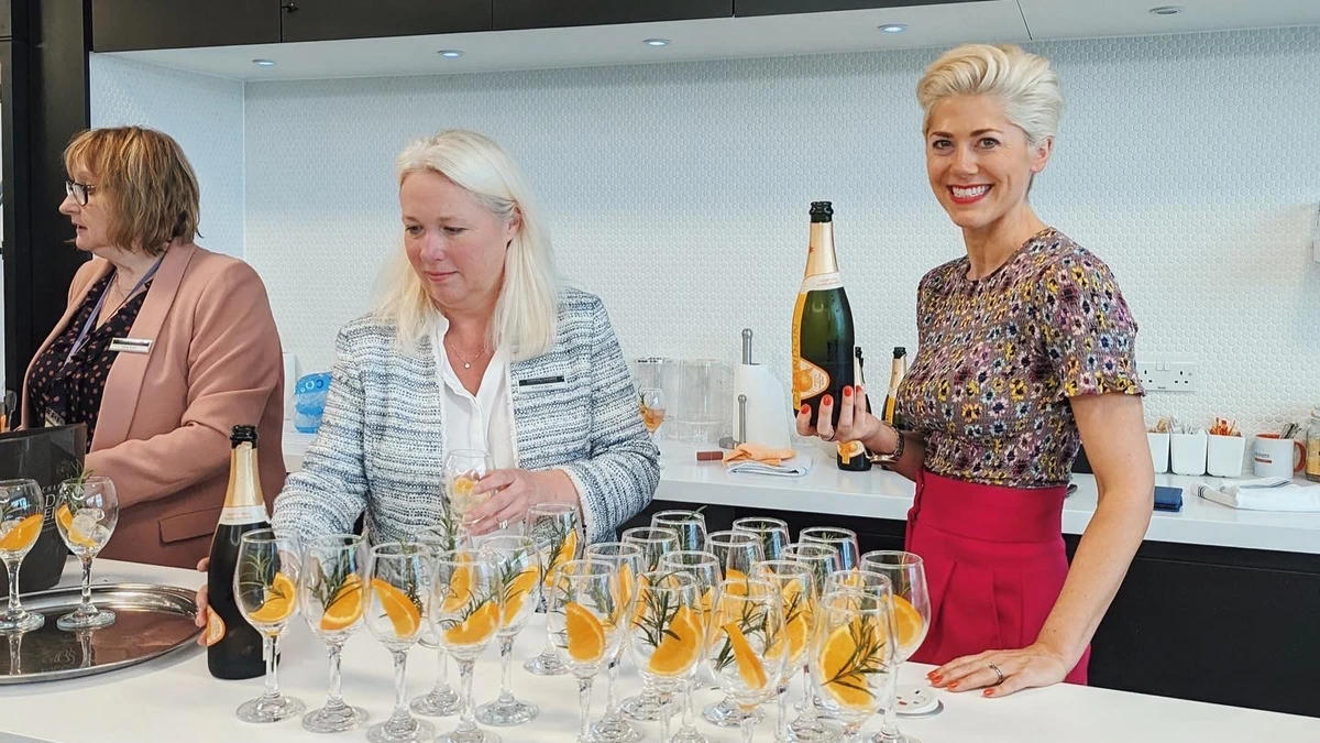 Three women serving champagne cocktails at a bar, with orange garnishes in glasses