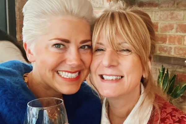 Two smiling women posing together, with a wine glass in the foreground