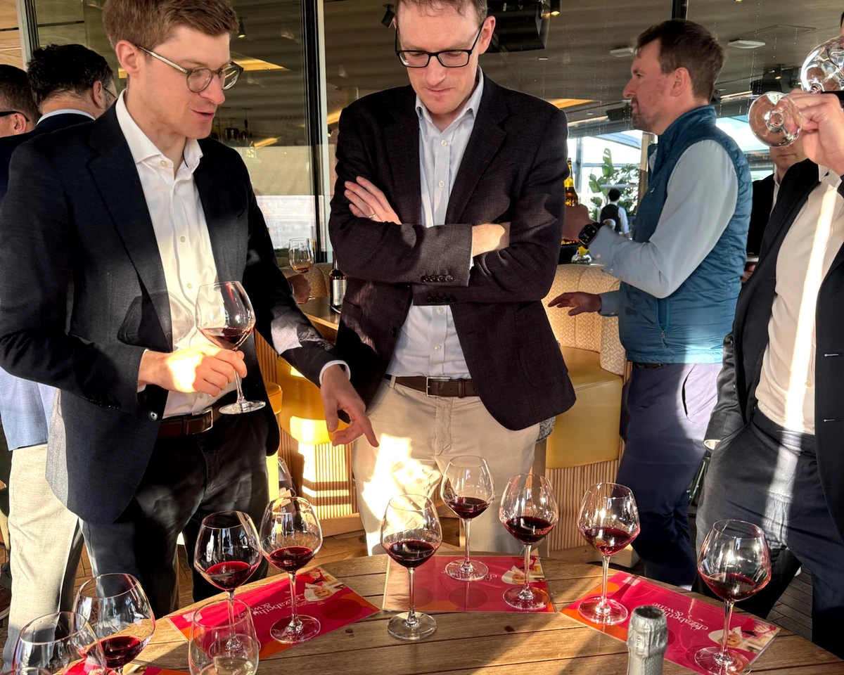People gather around a table of red wine glasses at a wine tasting event