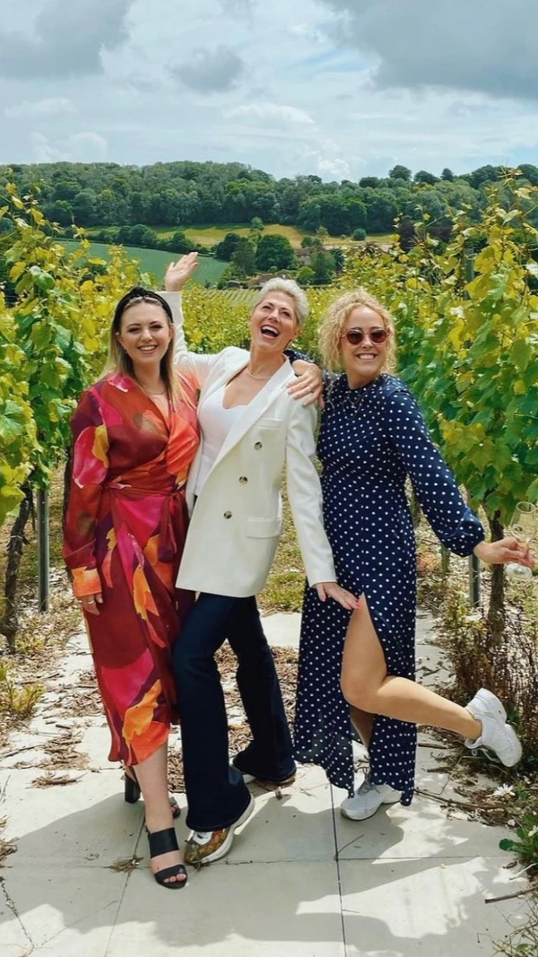 Three women posing among vineyard rows with rolling green hills behind them