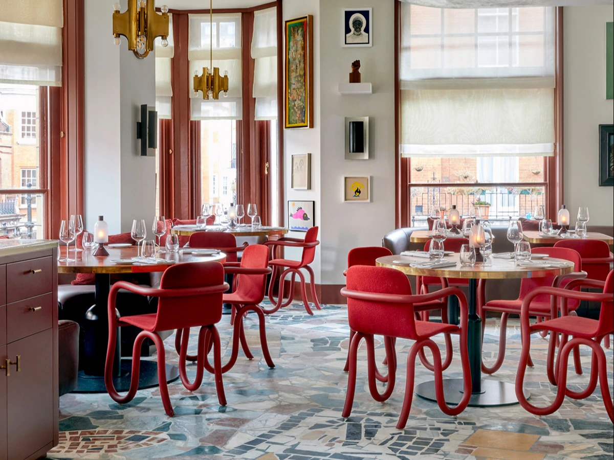 Bright restaurant interior with red chairs, set tables, chandeliers, artwork and large windows