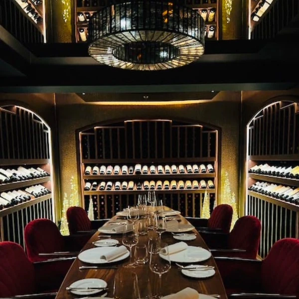 Wine cellar dining room with a long set table, red chairs and illuminated chandelier