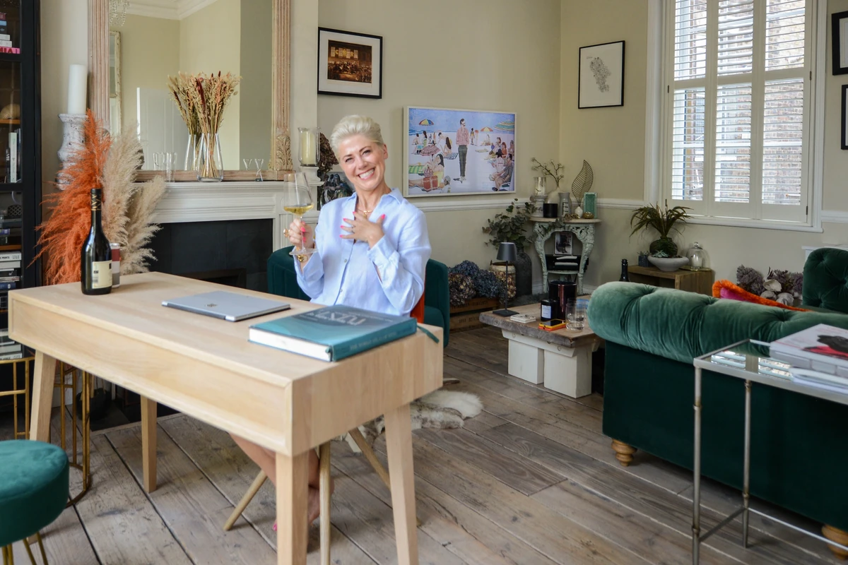 Woman holding a glass of wine in a stylish sitting room beside a desk