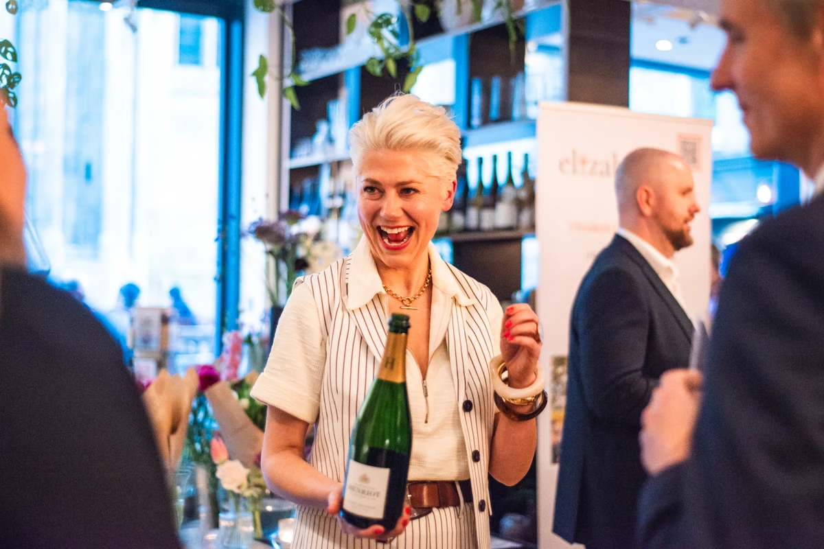 Smiling woman holding a wine bottle at a busy indoor event