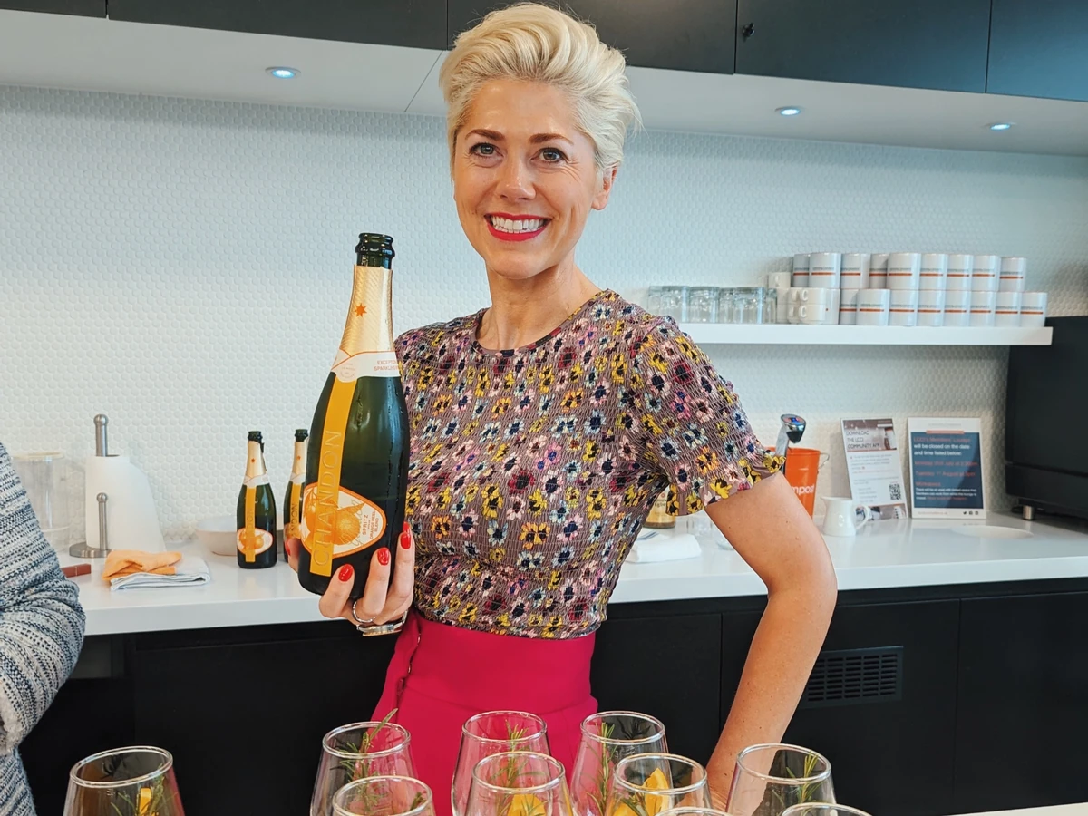 Smiling woman holding a bottle of champagne behind a table of wine glasses
