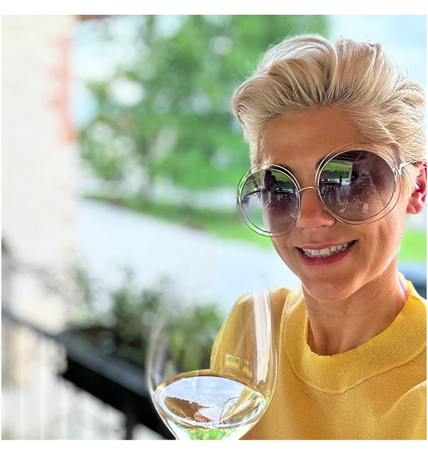 Smiling woman wearing round sunglasses and holding a glass of white wine