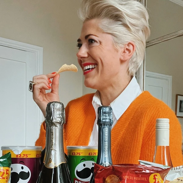 Smiling woman eating a crisp beside champagne bottles and snack packets
