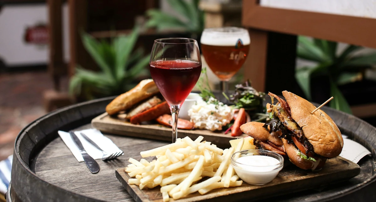 Burger and chips with dipping sauce, sharing platter, and two glasses of beer on a table