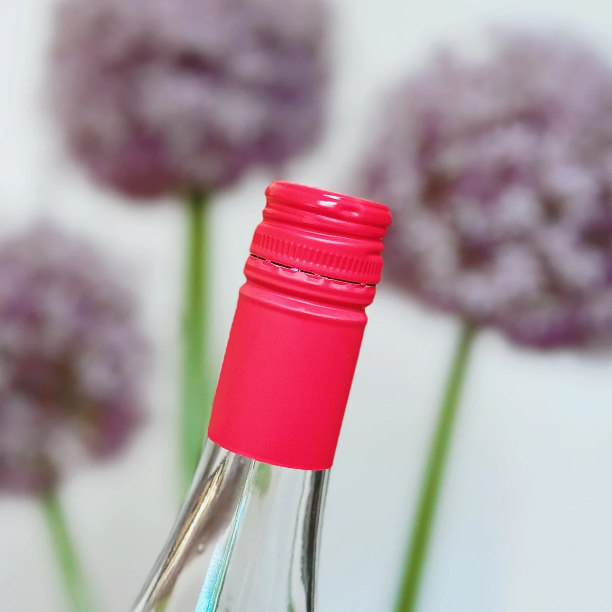 Close-up of a wine bottle with a bright pink screw cap and blurred flowers behind