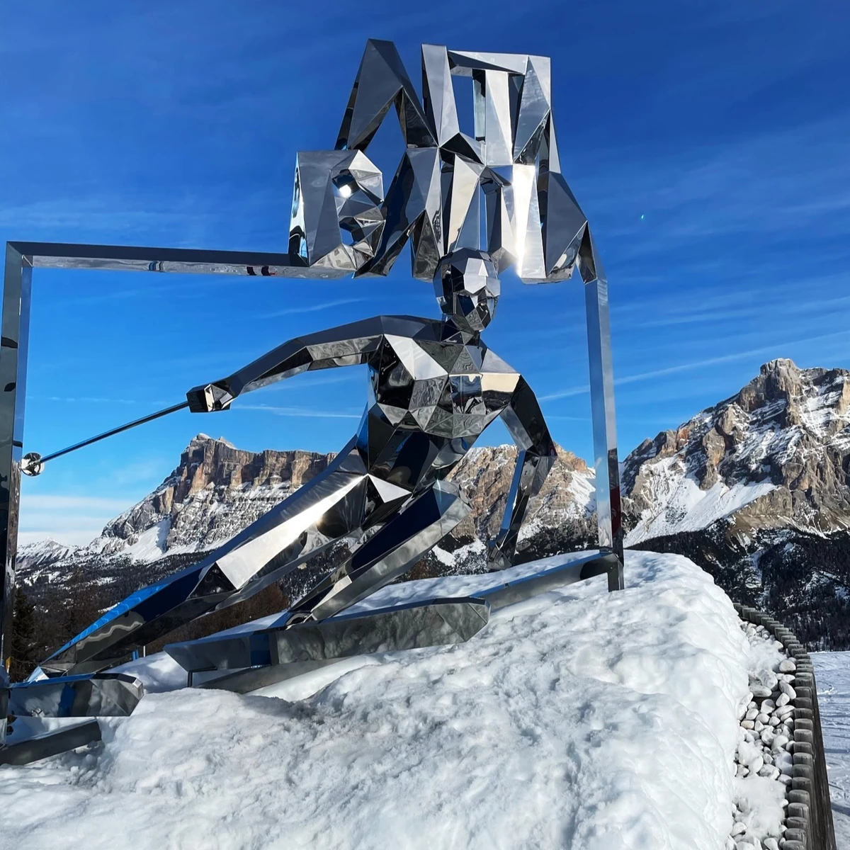 Reflective angular metal skier sculpture in snowy mountains under a clear blue sky