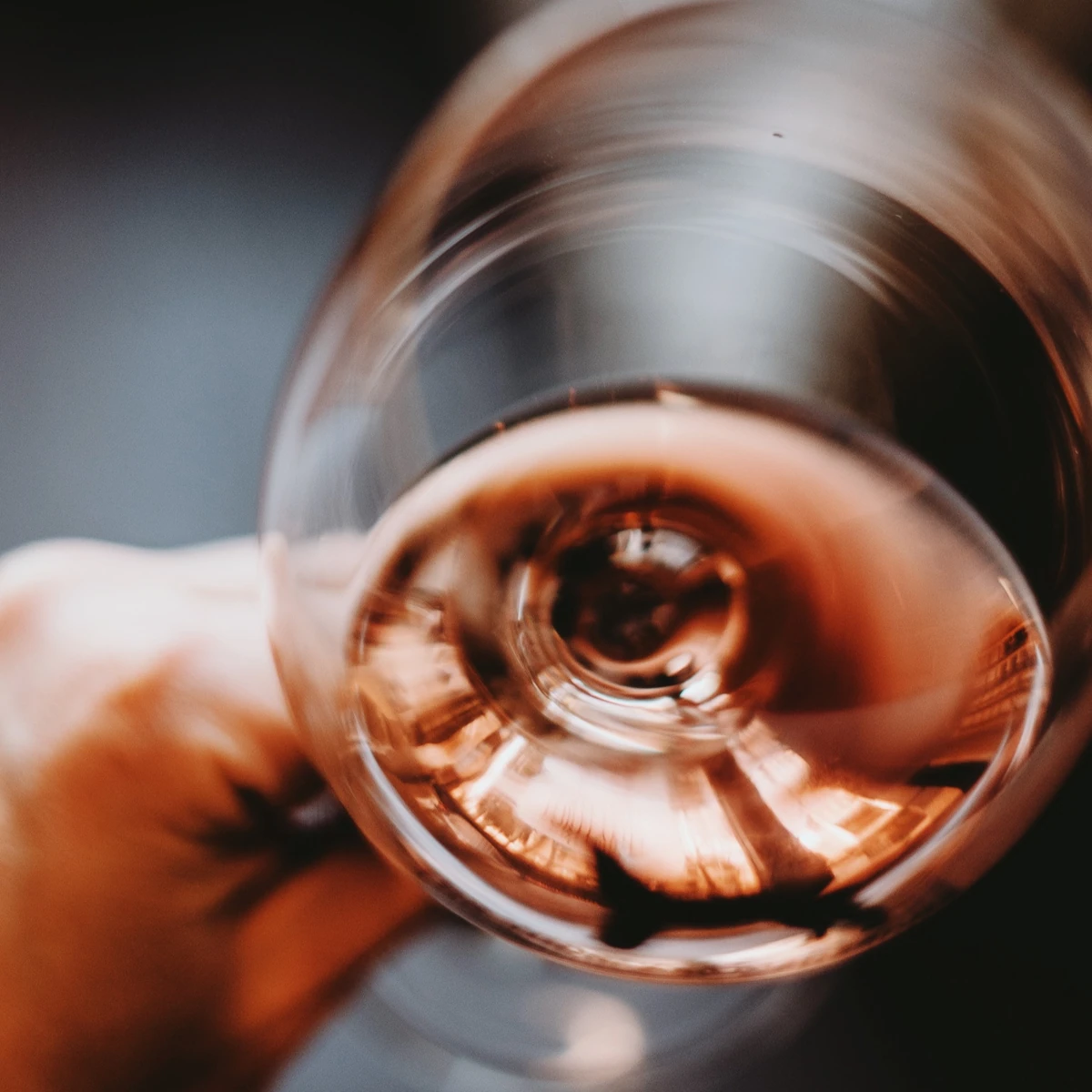 Close-up of a hand holding a tilted glass containing rosé wine