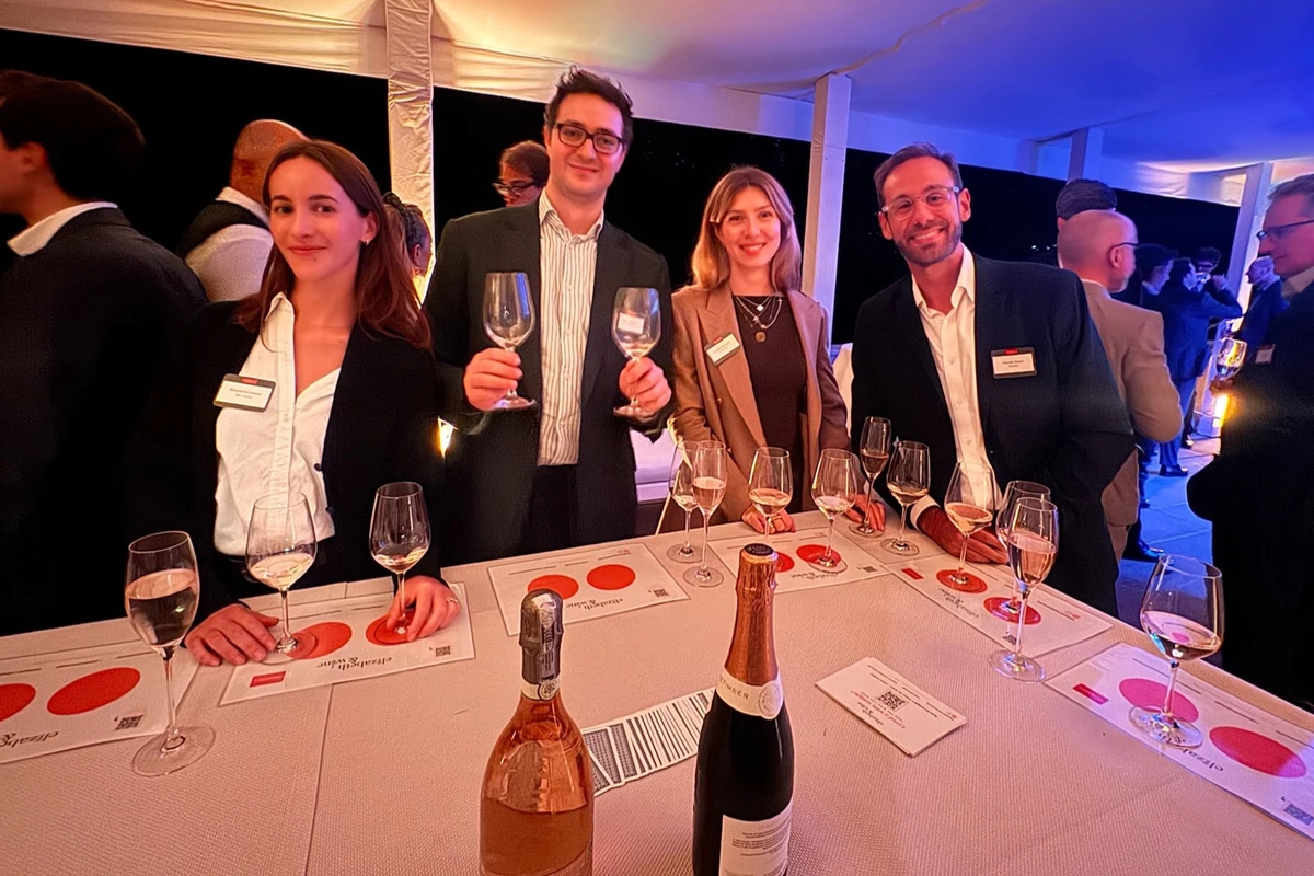 Four people posing at a wine tasting table with glasses and bottles